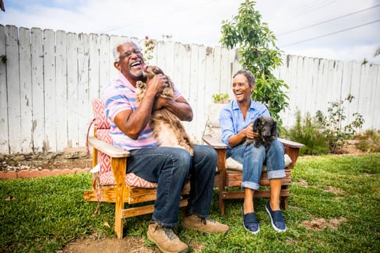 A couple sits in chairs outside with their two dogs