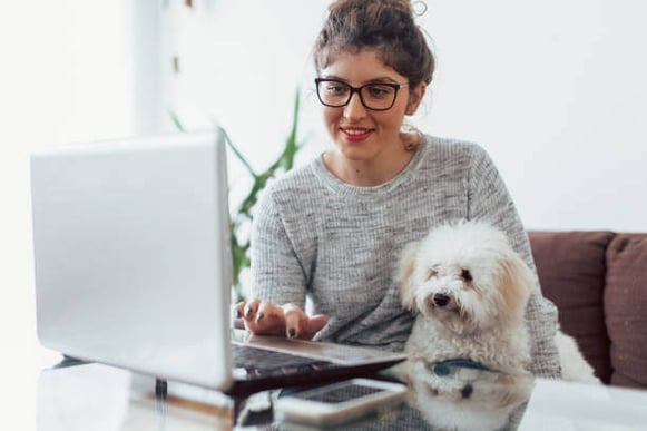 A woman uses her laptop while holding a dog