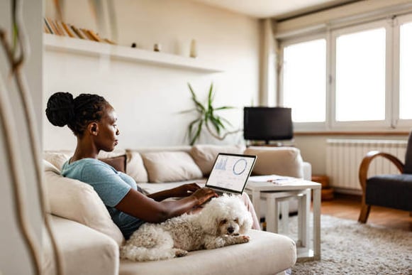 A woman looks at metrics on her laptop as her dog sits next to her.