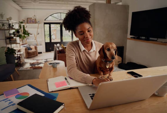 A woman uses a laptop as a dog sits on her lap