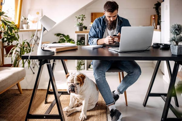 A man uses a phone while a dog sits at his feet