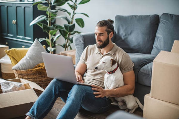 A man uses a laptop as a dog sits next to him