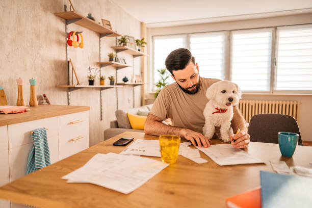 A man looks at papers on a table as a dog sits next to him