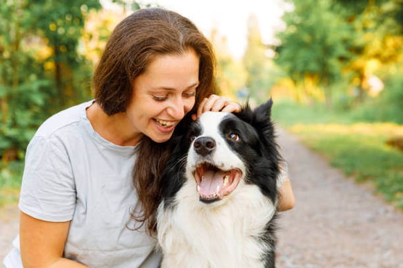 A woman smiles at a border collie dog as she pets it