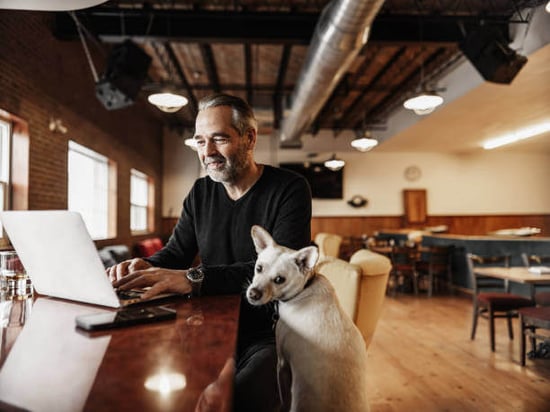 A man uses a laptop as a dog sits next to him