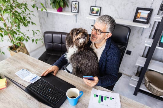 A man uses a computer as a dog sits on his lap