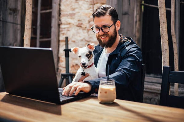 A man uses a laptop while holding a dog outside