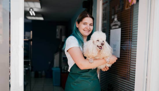 A woman groomer holds a dog in front of a pet business