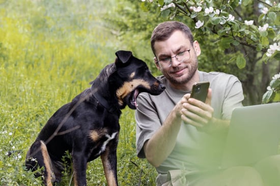 A man uses a phone outside next to his dog