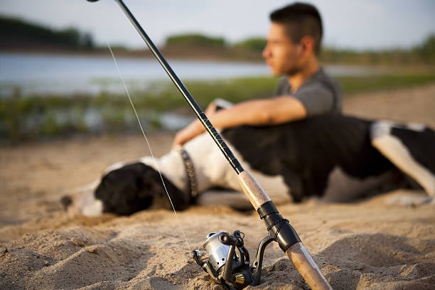 man fishing with sleepy dog on the beach