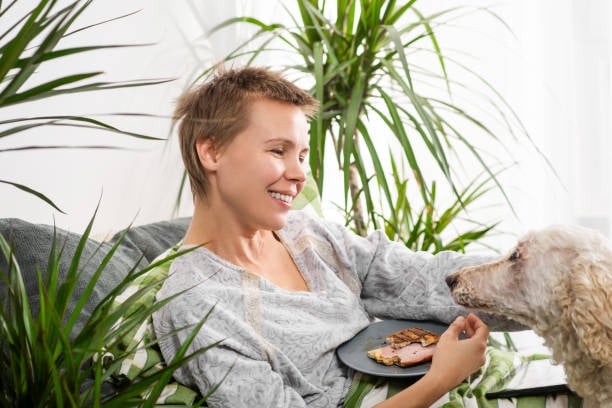 woman with plants feeding homemade food to dog