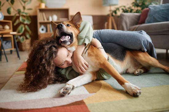 A woman hugs her dog while laying on the floor