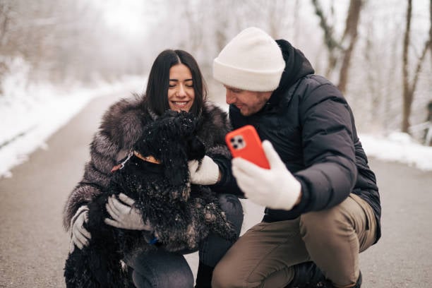 couple on phone outside in snow with dog