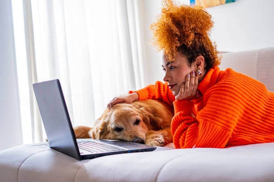 A woman uses a laptop as a dog sits next to her