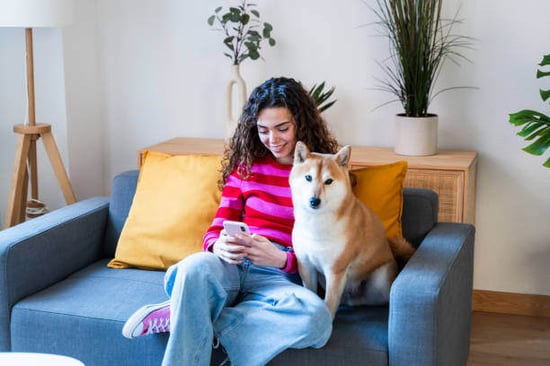 A woman sits next her dog on a couch while holding her phone