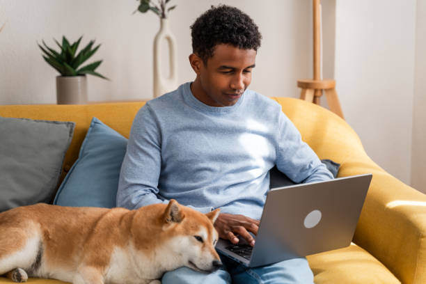A man uses a laptop as a dog sits next to him