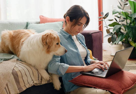 A woman uses a laptop as a dog sits next to her