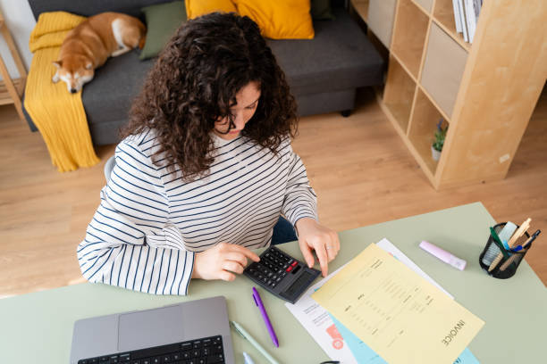 woman using paper invoices and calculator with sleeping dog on couch