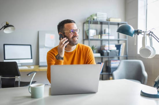A man talks on a phone while sitting at a desk