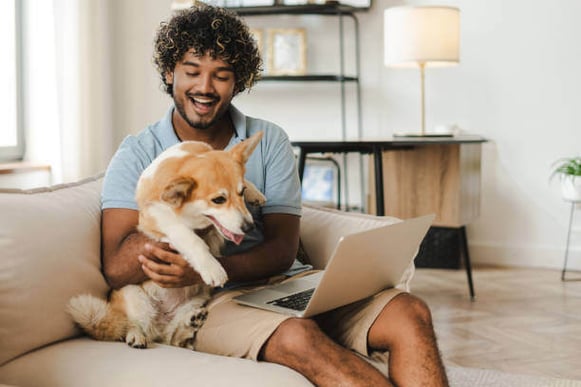 A man holds a corgi while sitting with a laptop