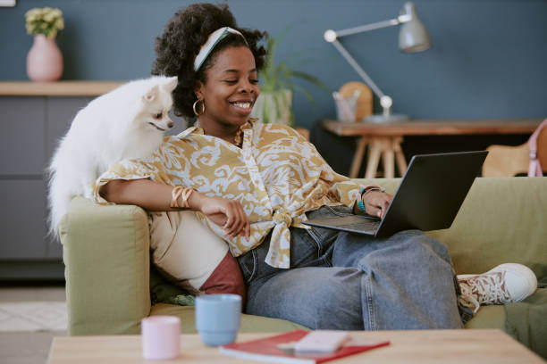 A woman uses a laptop as a dog sits next to her