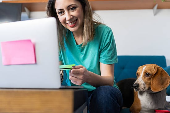 A woman uses a laptop as a dog sits next to her