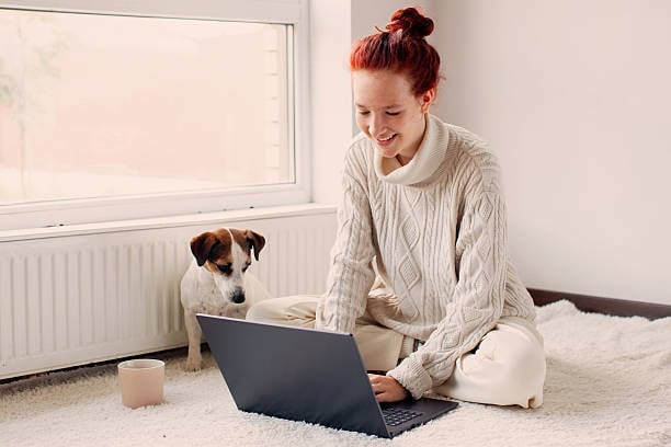 A woman uses a laptop as a dog sits next to her