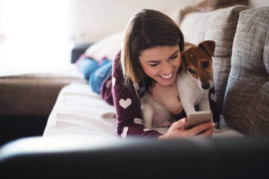 A woman uses a phone while hugging her dog
