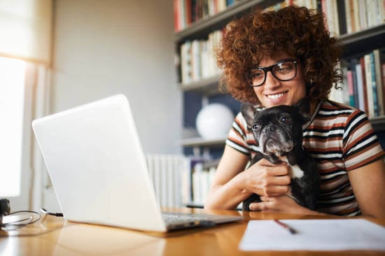 A woman uses a laptop as a dog sits on her lap